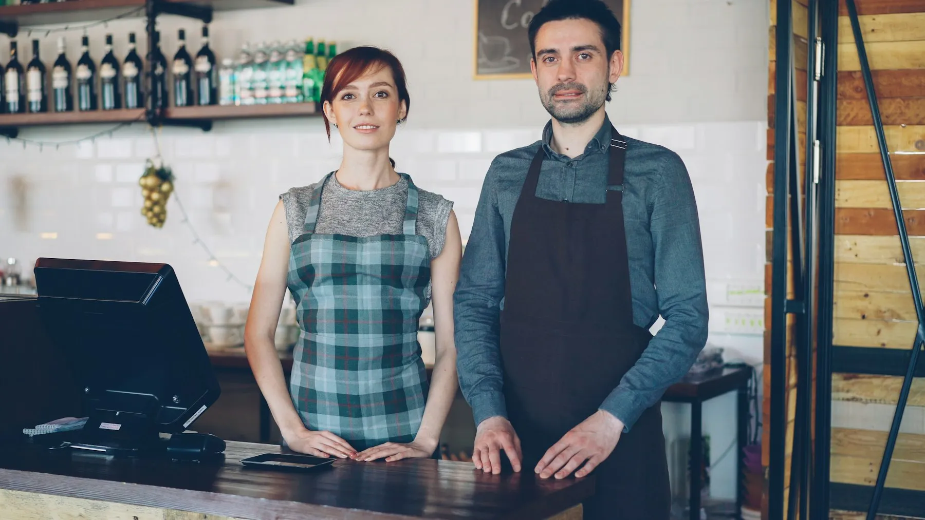 Two shop owners standing behind a counter with a till and laptop